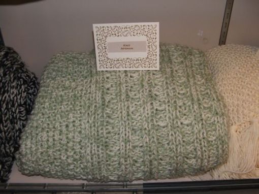 A closeup of the green knitted afghan that is using the same pattern as the cream on the right but 2 yarns to knit with at the same time.