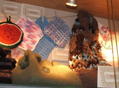 A closeup of some of the crocheted and knitted dishclothes and potholders, felted (knitted) purse, crocheted tote bag and a peek at the embroidered towels